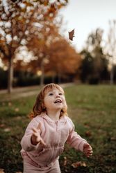 Joyful child scattering leaves on lawn in park