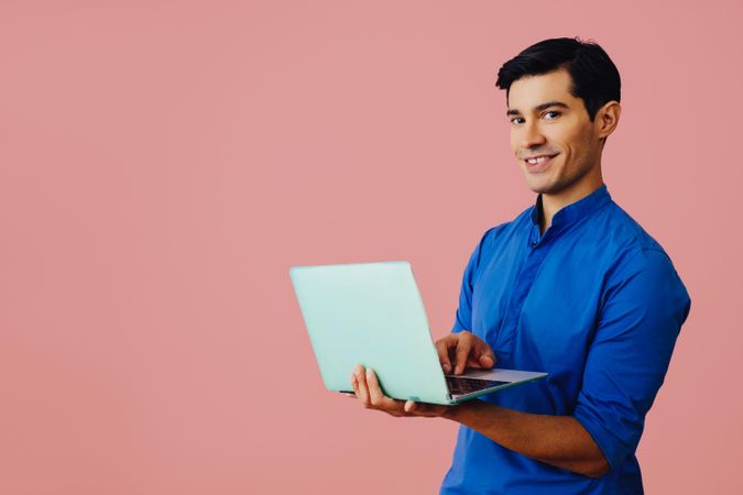 Latino man holding laptop in pink room, copy space