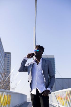 Black man in suit standing in city talking on phone on a sunny day