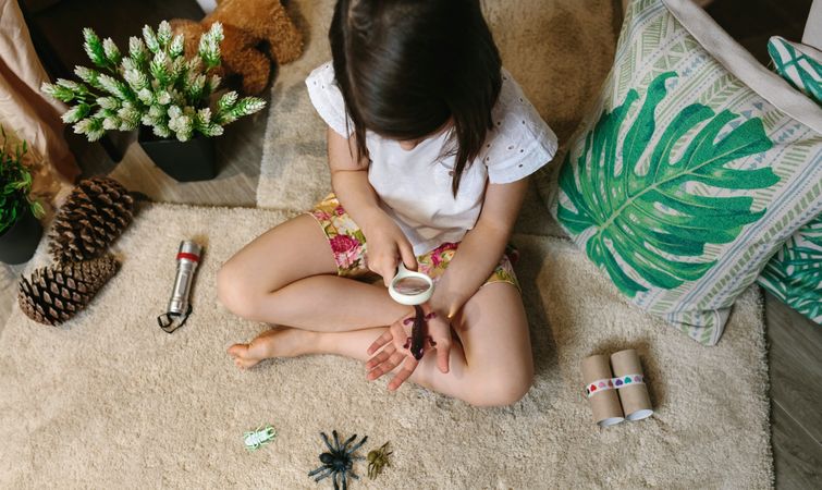 Girl playing observing toy bugs with a magnifying glass