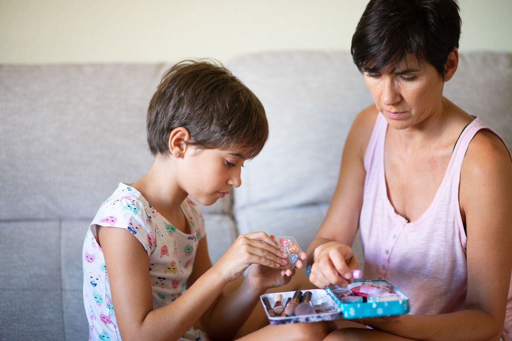 Little girl playing with make up brushes with her mother