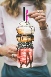 Woman holding stacked donut milkshake with straws, whipped cream, and chocolate sprinkles