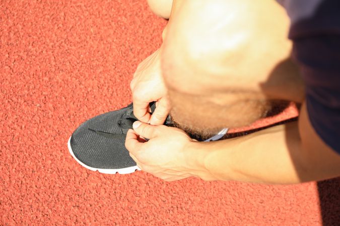 Man tying shoelaces on red athletic running track, close up