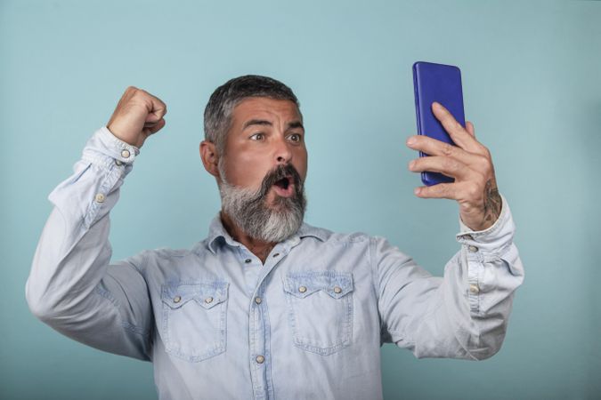 Excited man holding smartphone against blue background