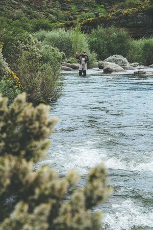 Confident man fishing with rod while standing in river stream