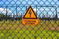 Sign showing the words high voltage in german language at the fence of a big substation distributing electric energy with lots power lines on a sunny day