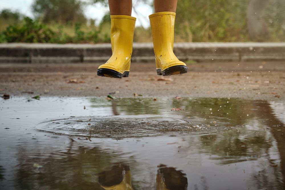 Unrecognizable kid in gumboots jumping in puddle