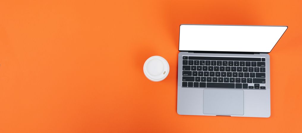 Banner of laptop on orange desk with take away cup of coffee or tea with copy space