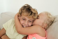 Loving sister kissing boy on sofa at home