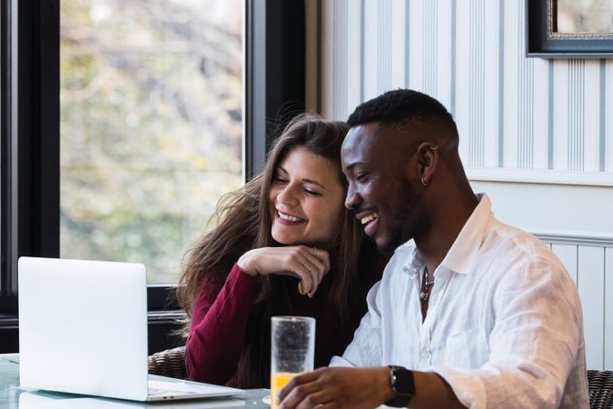 Cheerful multiethnic couple using laptop during breakfast at home