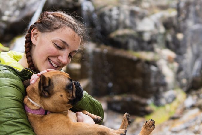 Cheerful traveling woman with dog near waterfall in forest