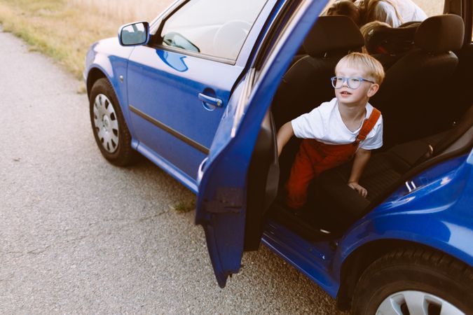 Happy little child in blue car park on asphalt road in countryside
