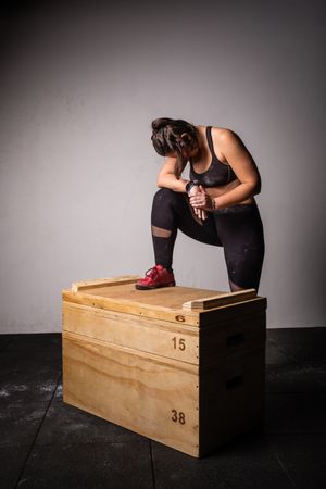 Woman jumping on wooden box in gym
