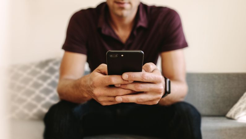 Cropped shot of man using smart phone while sitting on couch