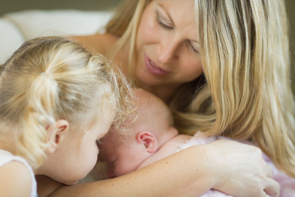 Happy New Mom Holds Newborn Baby Girl with Young Sister