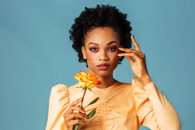 Studio shot of a Black woman holding a yellow rose with her hand to her temple