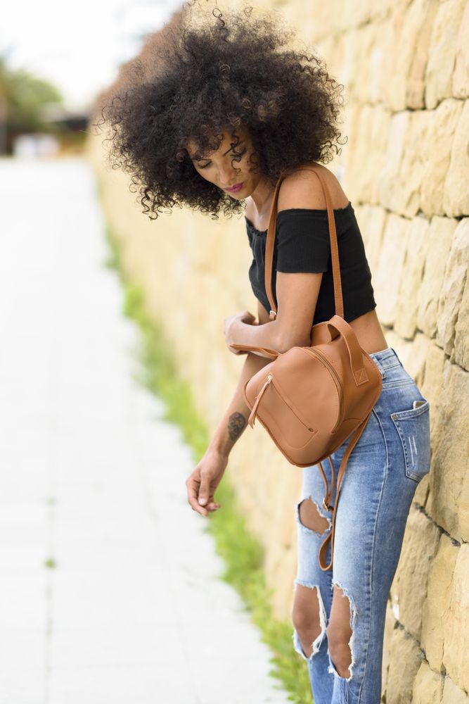 Female standing on street looking down while leaning on wall