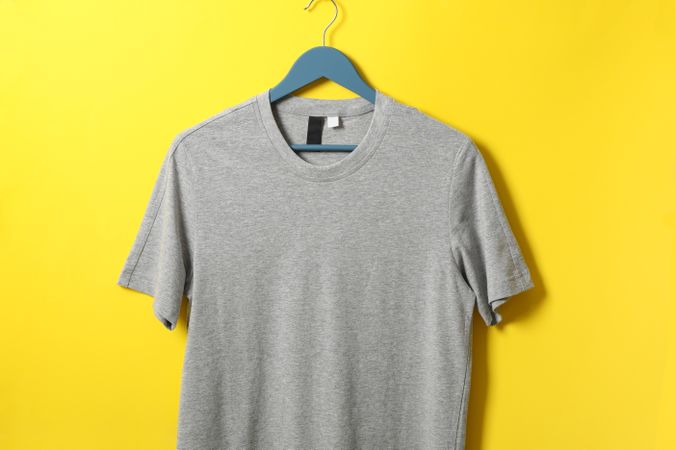 Hanger with blank gray t-shirt on yellow background, space for text
