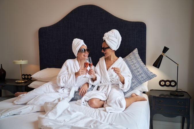 Happy women clinking glasses of champagne resting on bed