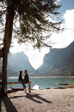 Male and female travelers sitting on fence near lake and mountains