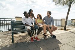Group of young multicultural friends talking on a bench by the sea.