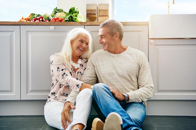 Calm older couple smiling while sitting on the kitchen floor