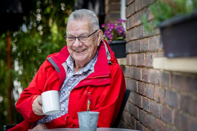 Smiling older man sitting with coffee mug with a red jacket