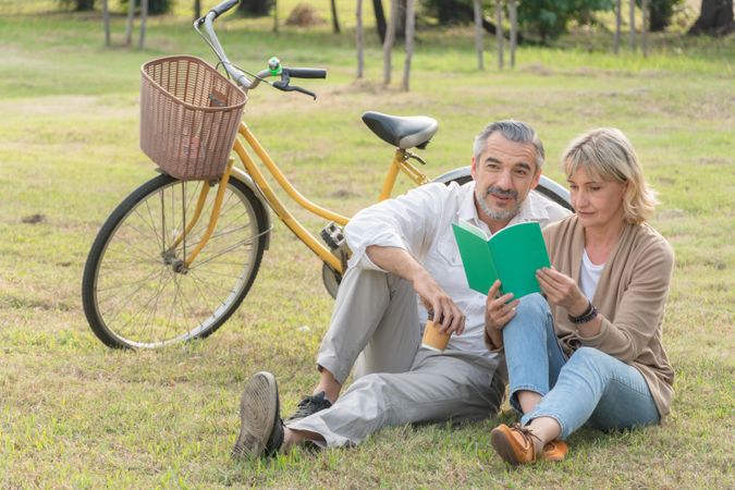 Mature male and female sitting in the grass in public park with bicycle