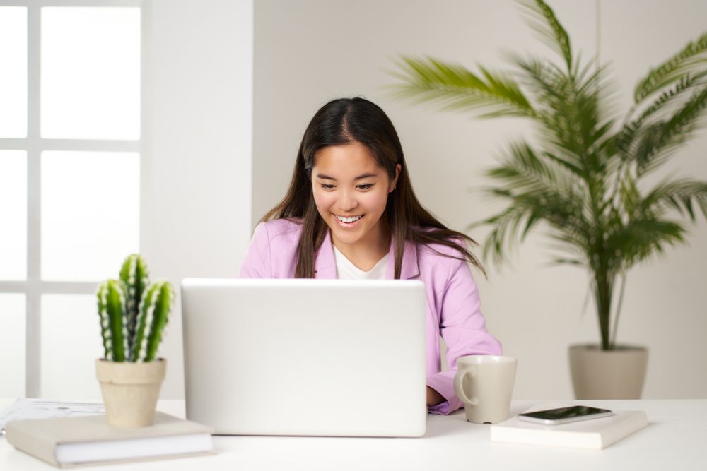 a young asian woman smiling and looking at the computer in the coworking space