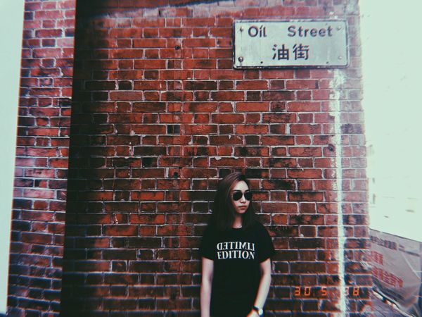 Woman in dark t-shirt standing beside brick wall
