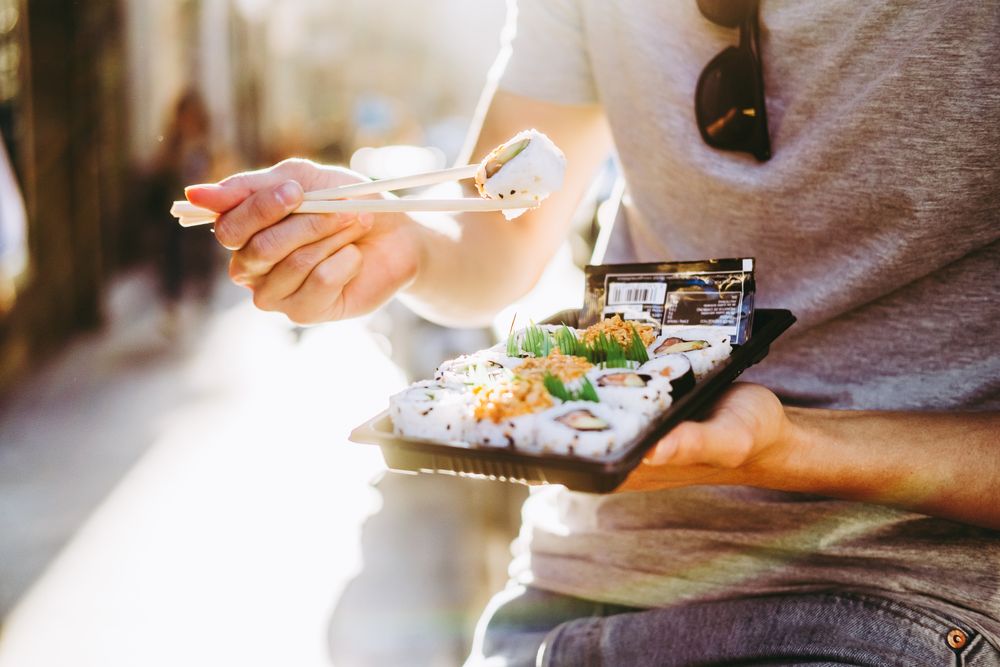 Asian man eating takeaway food with chopsticks on city street