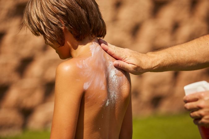 Faceless man applying sun cream on kid