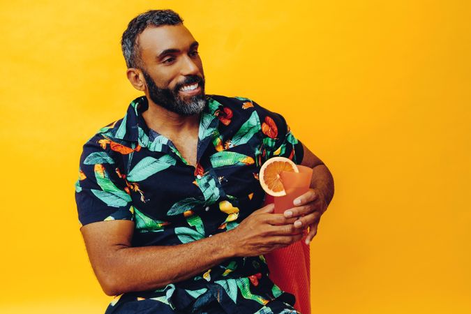 Happy Black male sitting down with cocktail in yellow room, copy space