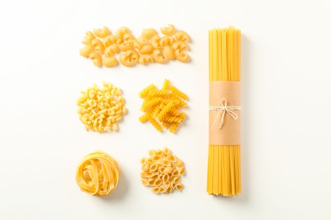 Flat lay composition with different pasta on light background, space for text