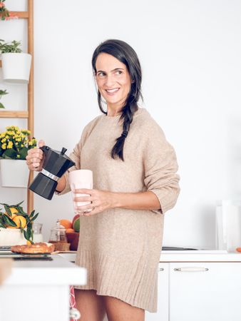 Smiling female pouring coffee from moka pot in kitchen