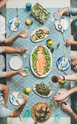 Group of people at blue patterned table with fish, and vegetable side dishes, vertical composition