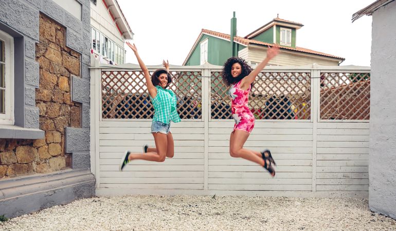 Two female friends facing each other and jumping in backyard