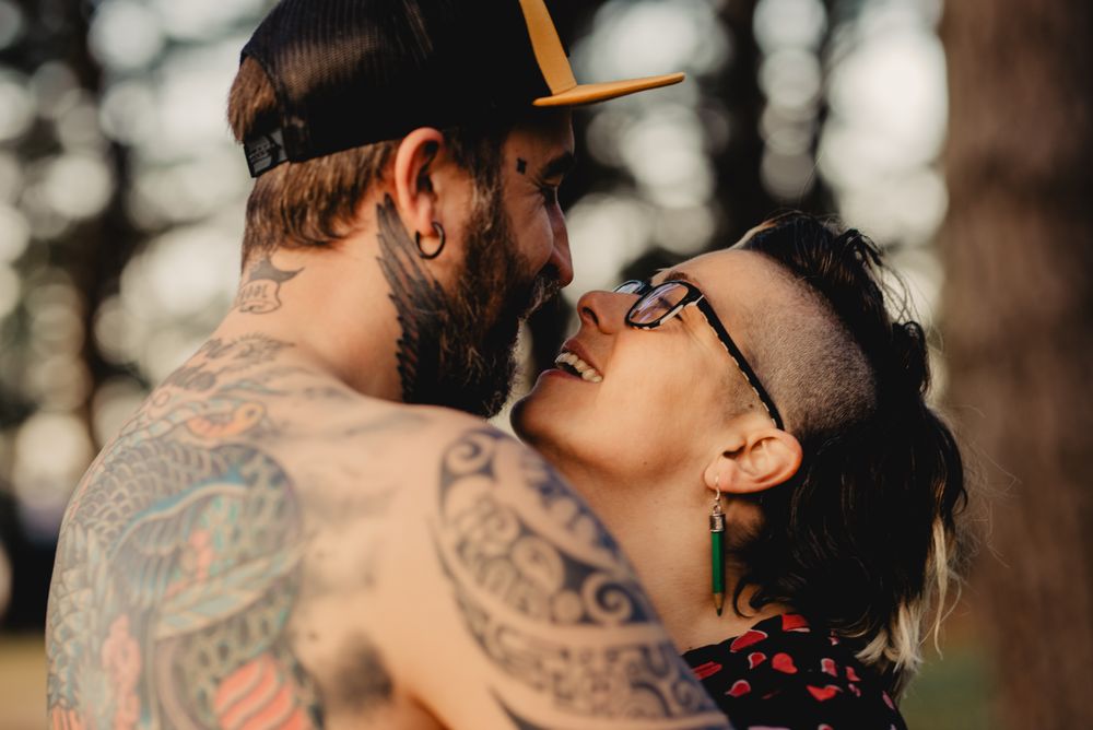 Young guy in tattoos hugging woman in forest