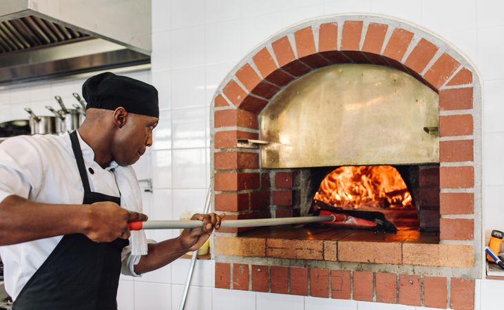 Chef baking pizza in the wood fire oven at commercial kitchen