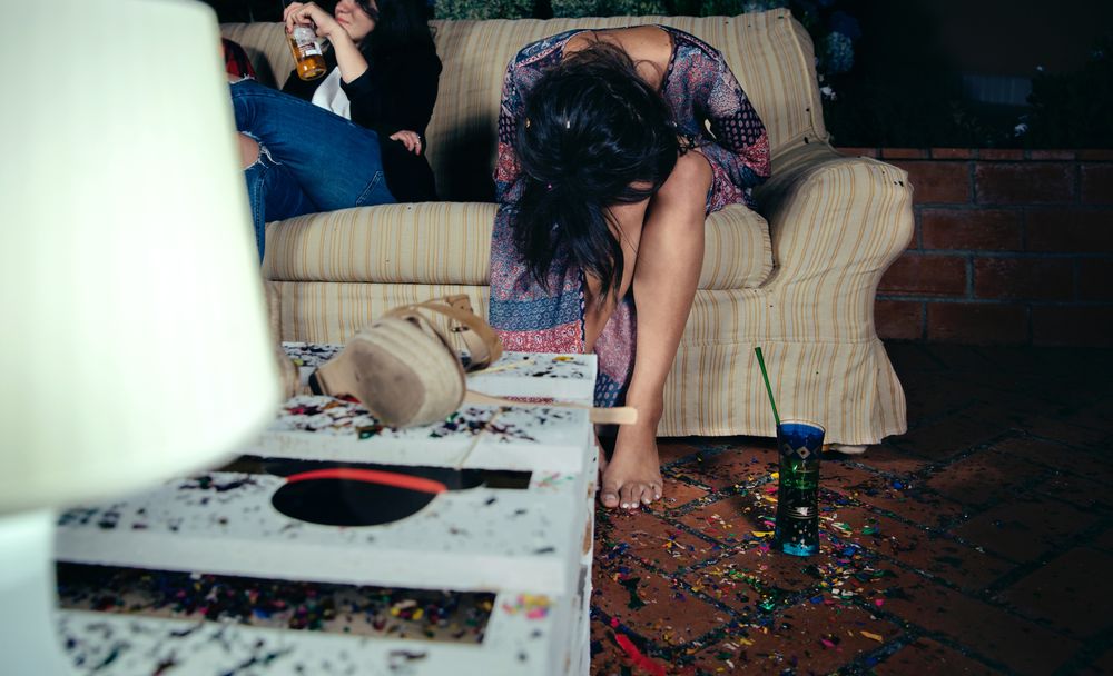 Young inebriated woman sitting on the sofa on a party with her head in her lap