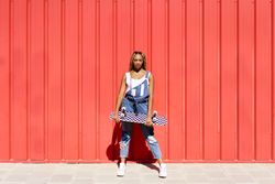 Woman leaning against red wall with checkered skateboard