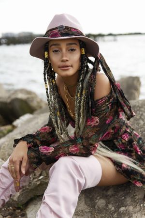 Woman with dreads and hat sitting on beach