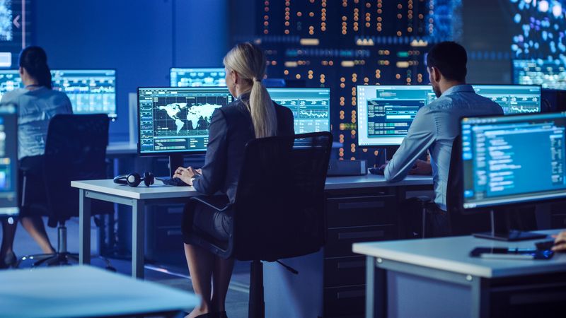 Diverse Team in a High-tech Control Room Monitors Global Data on Multiple Screens, Focusing on Cybersecurity and Network Optimization for Seamless Digital Operations.