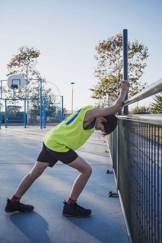 Young basketball player stretching legs before playing game outdoors