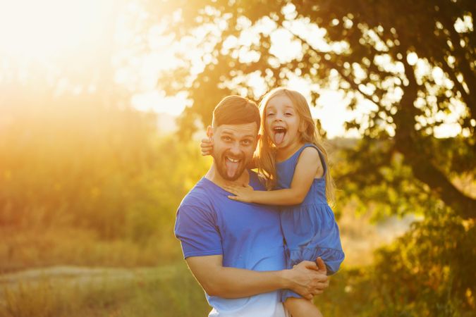 Man with daughter in sunny meadow making funny face