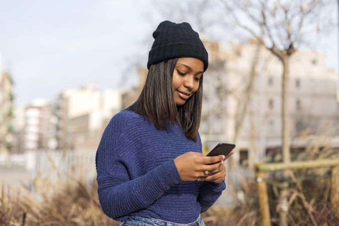 Woman in sweater checking smart phone outside