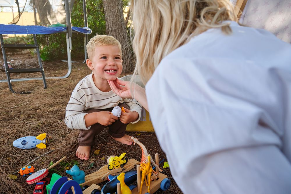 Happy child playing with toys near mother in park