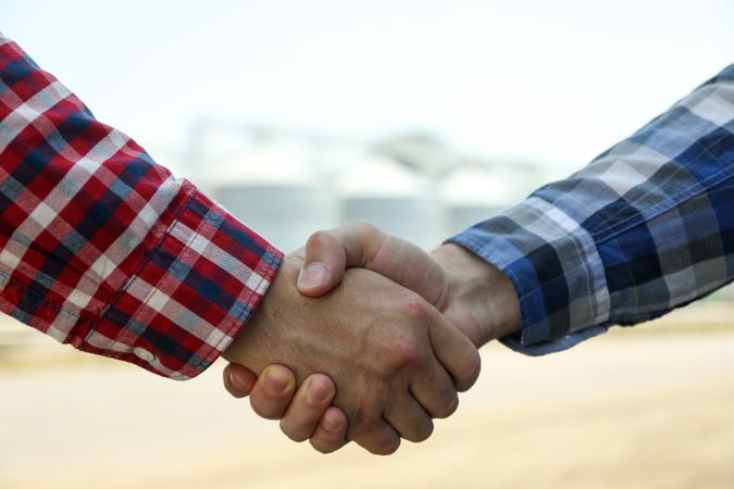 Businessmen shake hands against silos. Agriculture business