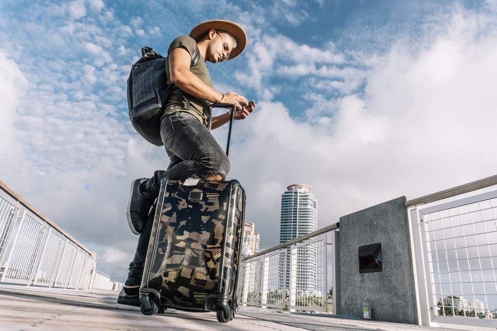 Traveller man texting phone with his luggage walking on Ocean drive South Beach Florida
