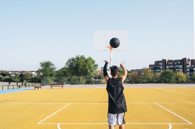 Young man playing on yellow basketball court outdoor.